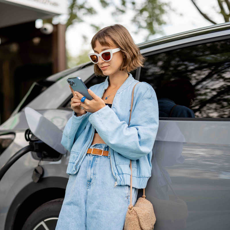 Junge Frau steht an einem E-Auto während es lädt