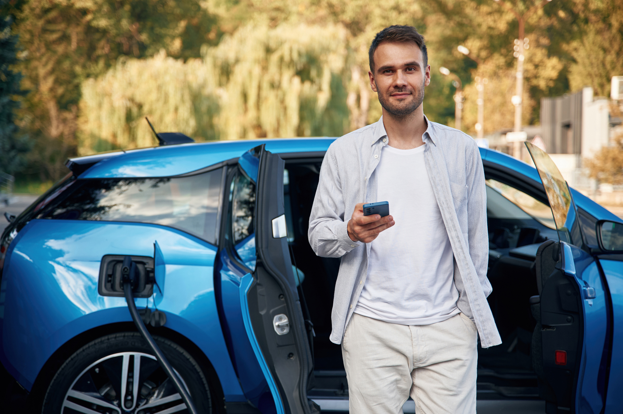 Mann vor einem blauen E-Auto steht an einer Ladestation. Mann vor einem blauen E-Auto steht an einer Ladestation.